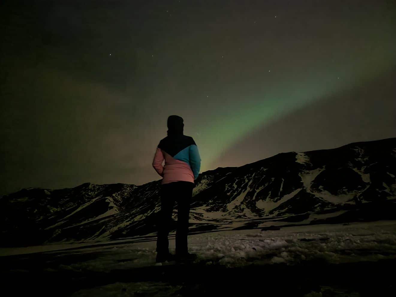 Frau in Winterjacke bewundert die Nordlichter Islands